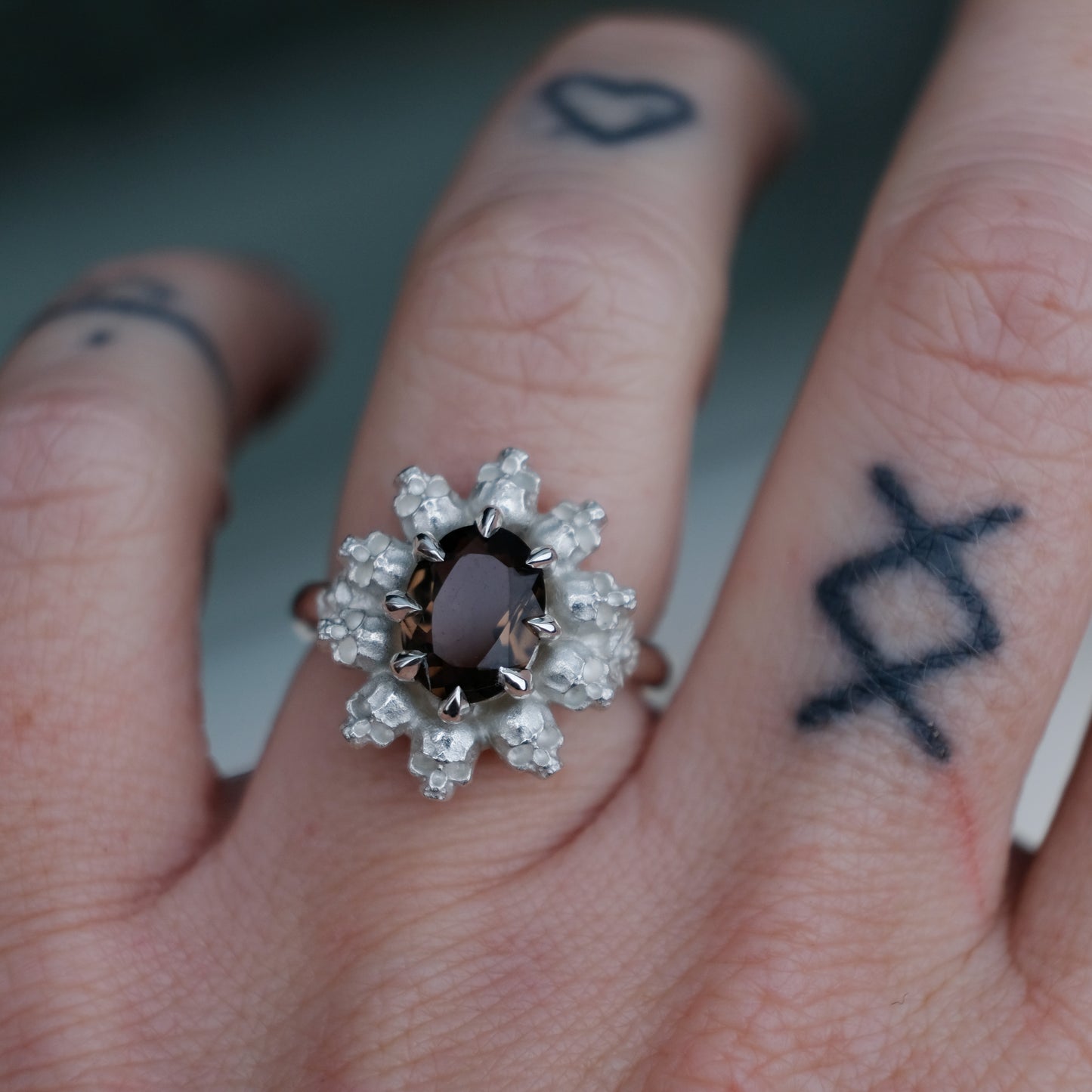 Silver ring with brown smokey quartz gemstone in skull halo design worn on hand with tattoos handmade in London, UK
