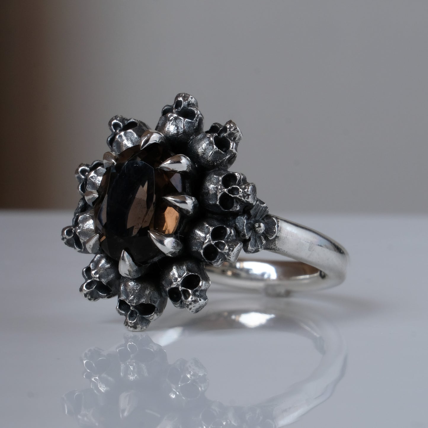 Silver ring with brown smokey quartz gemstone in skull halo design on reflective background handmade in London, UK