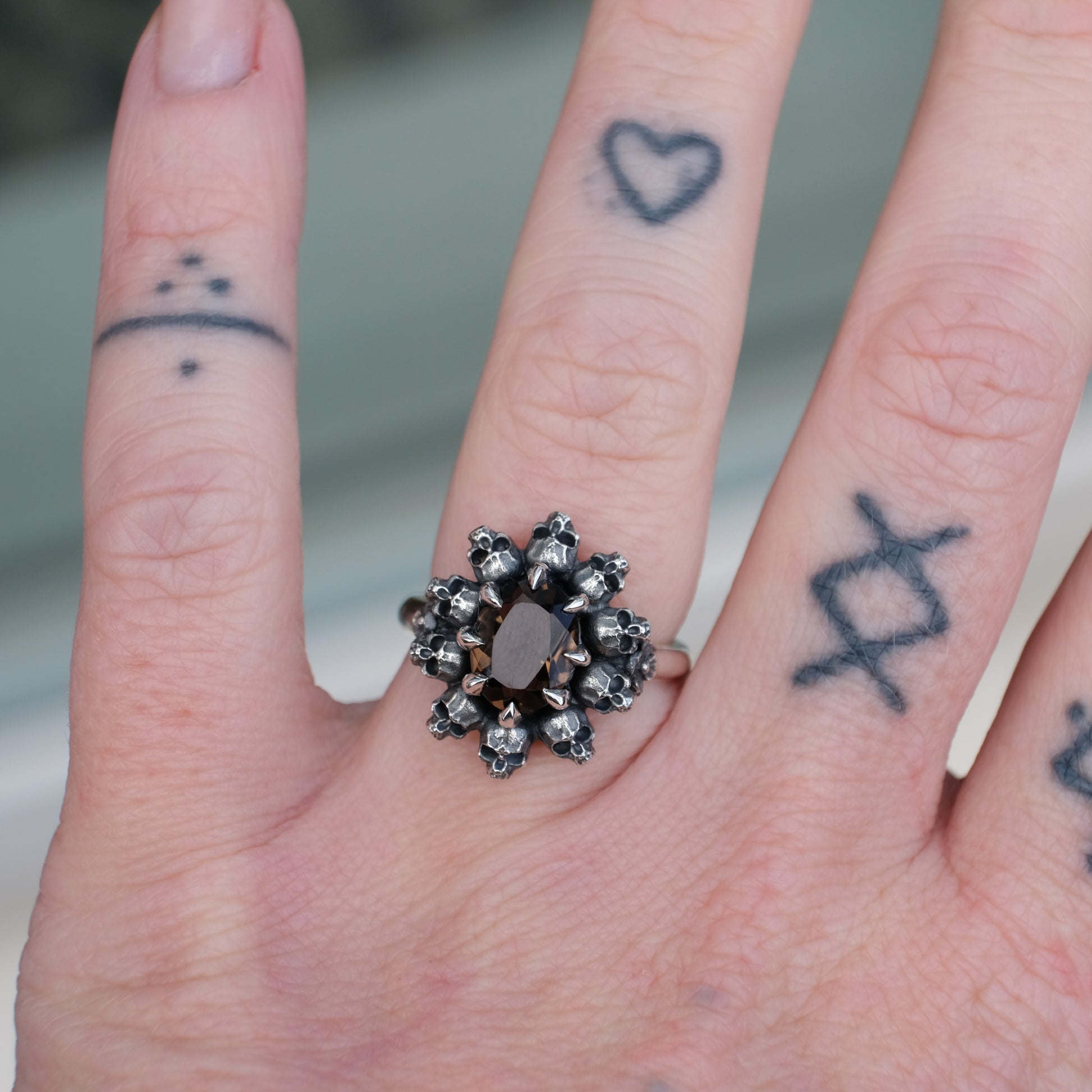 Silver ring with brown smokey quartz gemstone in skull halo design worn on hand with tattoos handmade in London, UK