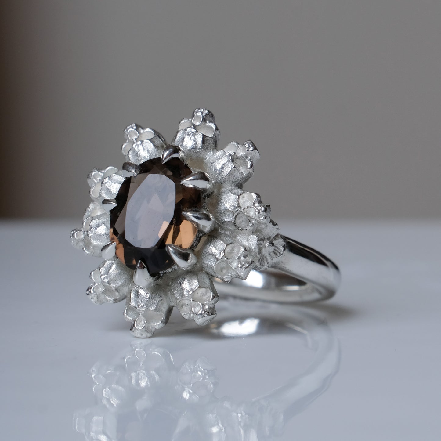 Silver ring with brown smokey quartz gemstone in skull halo design on reflective background handmade in London, UK