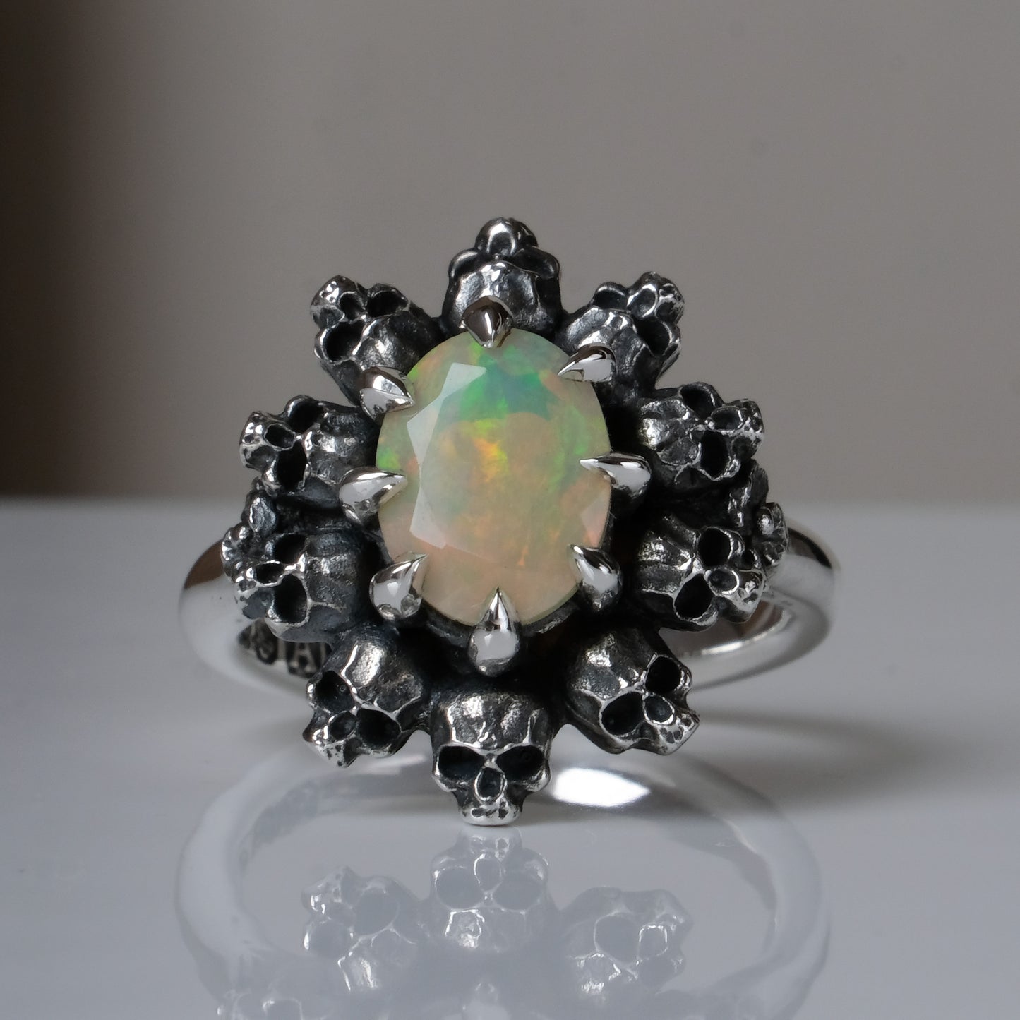 Silver ring with white opal gemstone in skull halo design on reflective background handmade in London, UK