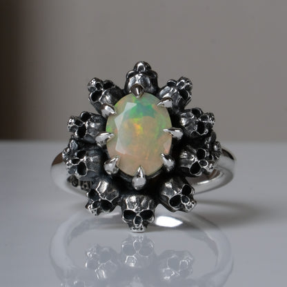 Silver ring with white opal gemstone in skull halo design on reflective background handmade in London, UK