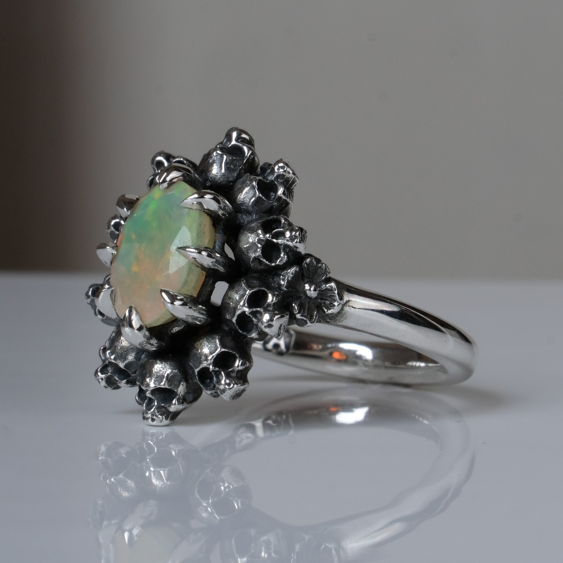 Silver ring with white opal gemstone in skull halo design on reflective background handmade in London, UK