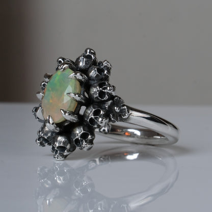Silver ring with white opal gemstone in skull halo design on reflective background handmade in London, UK