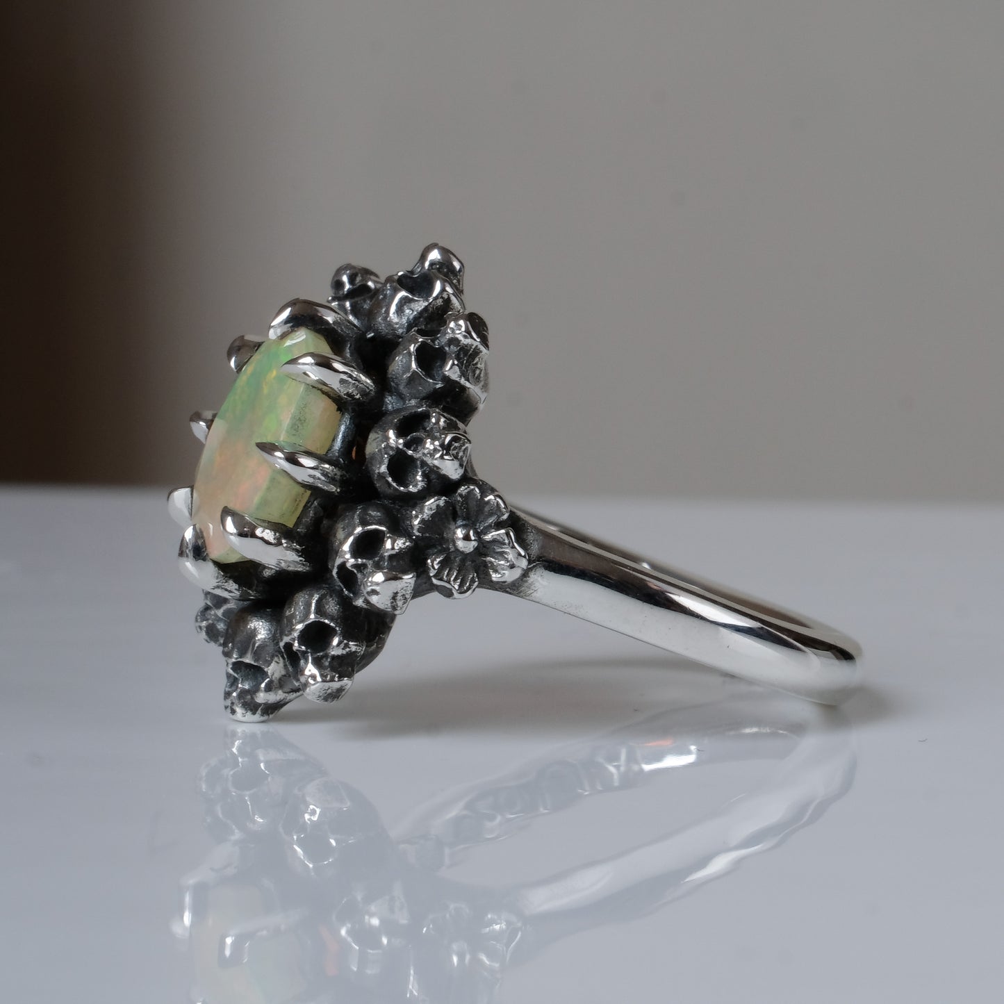 Silver ring with white opal gemstone in skull halo design on reflective background handmade in London, UK
