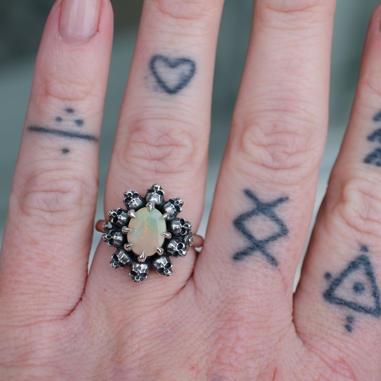 Silver ring with white opal gemstone in skull halo design worn on hand with tattoos handmade in London, UK