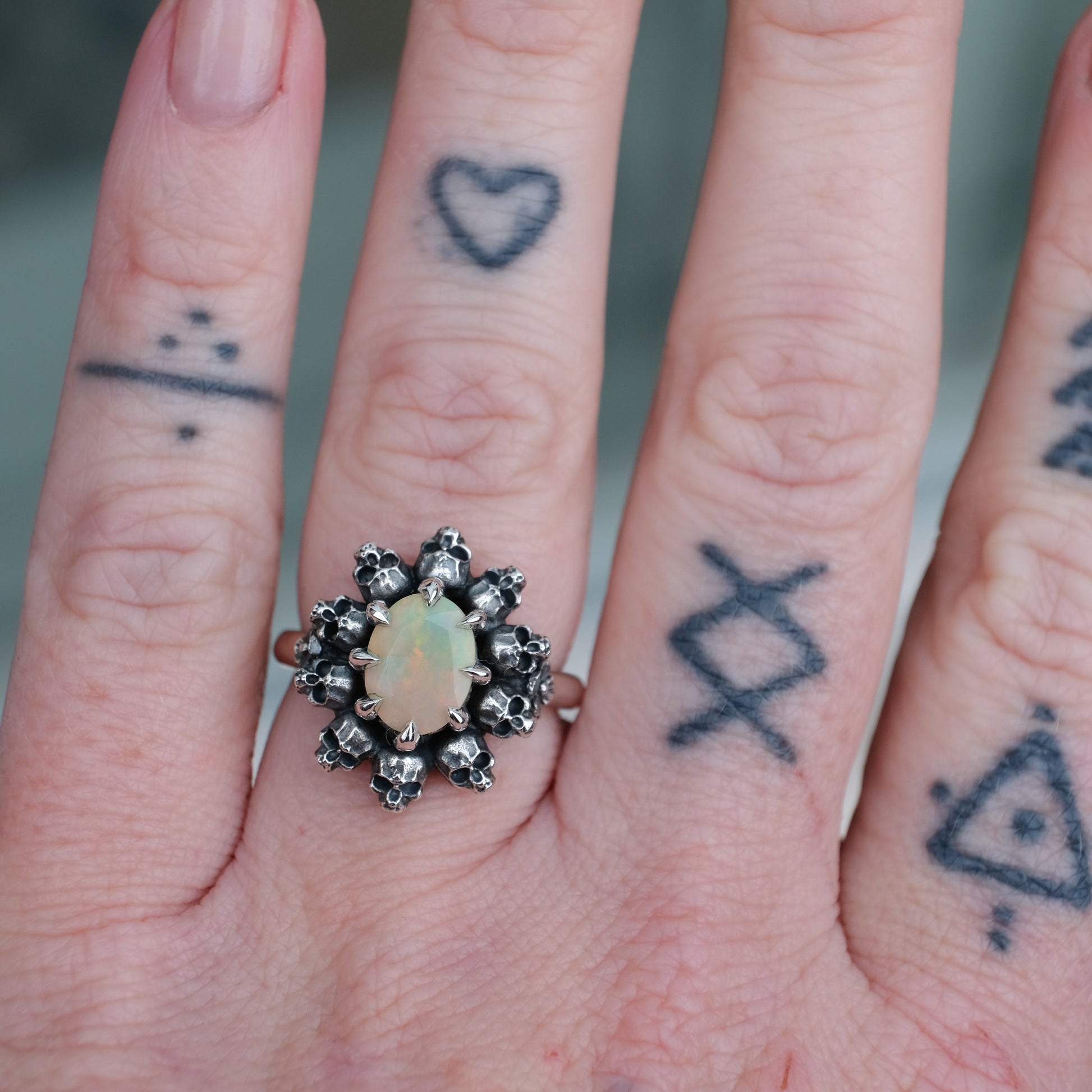 Silver ring with white opal gemstone in skull halo design worn on hand with tattoos handmade in London, UK