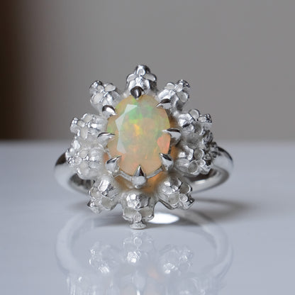 Silver ring with white opal gemstone in skull halo design on reflective background handmade in London, UK