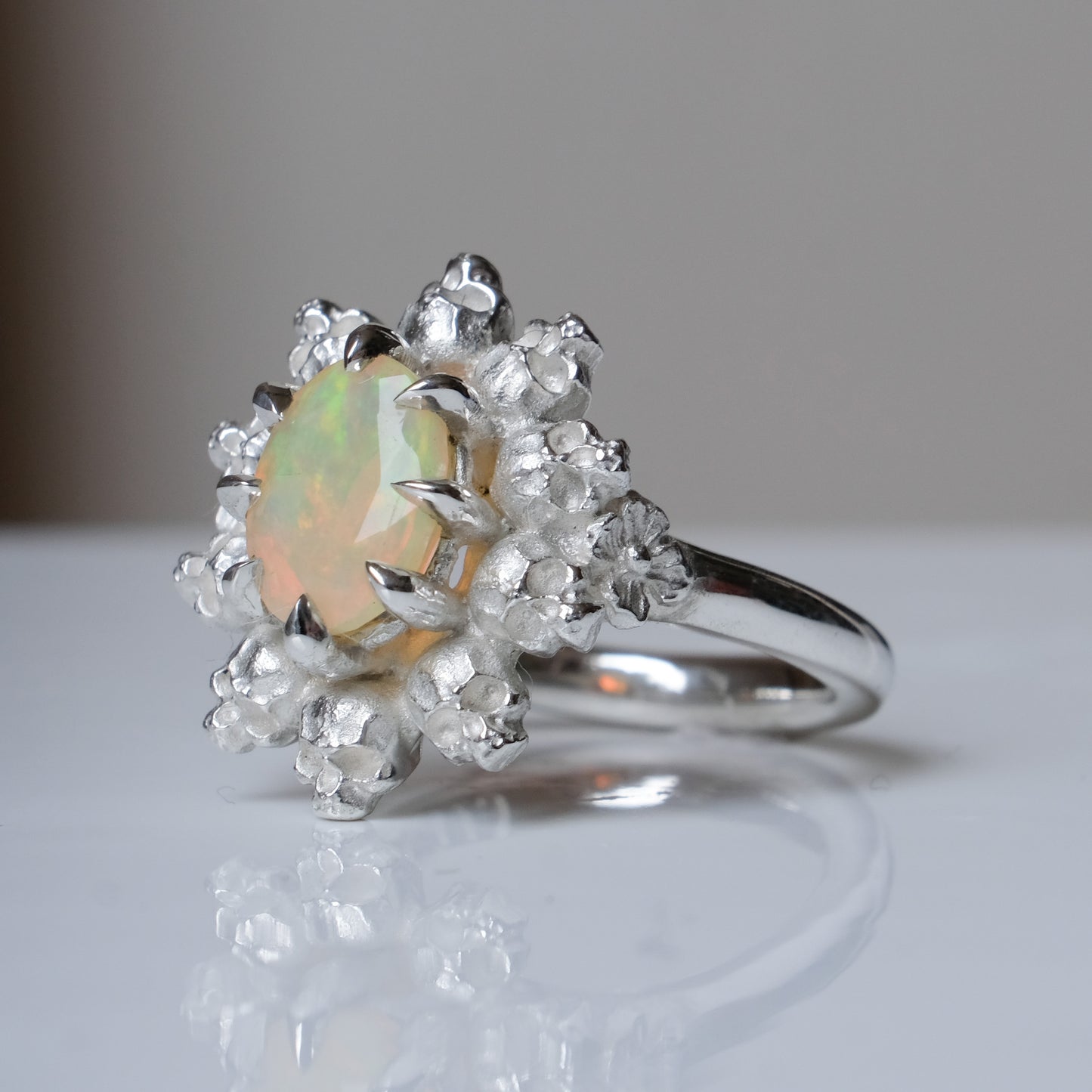 Silver ring with white opal gemstone in skull halo design on reflective background handmade in London, UK