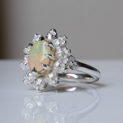 Silver ring with white opal gemstone in skull halo design on reflective background handmade in London, UK