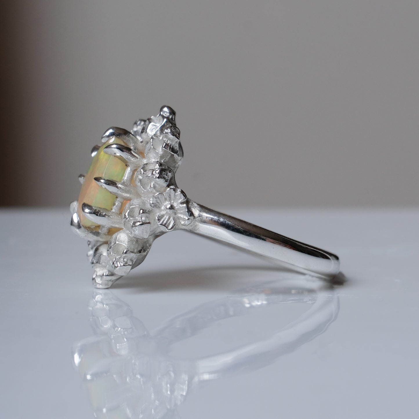 Silver ring with white opal gemstone in skull halo design on reflective background handmade in London, UK