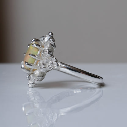 Silver ring with white opal gemstone in skull halo design on reflective background handmade in London, UK