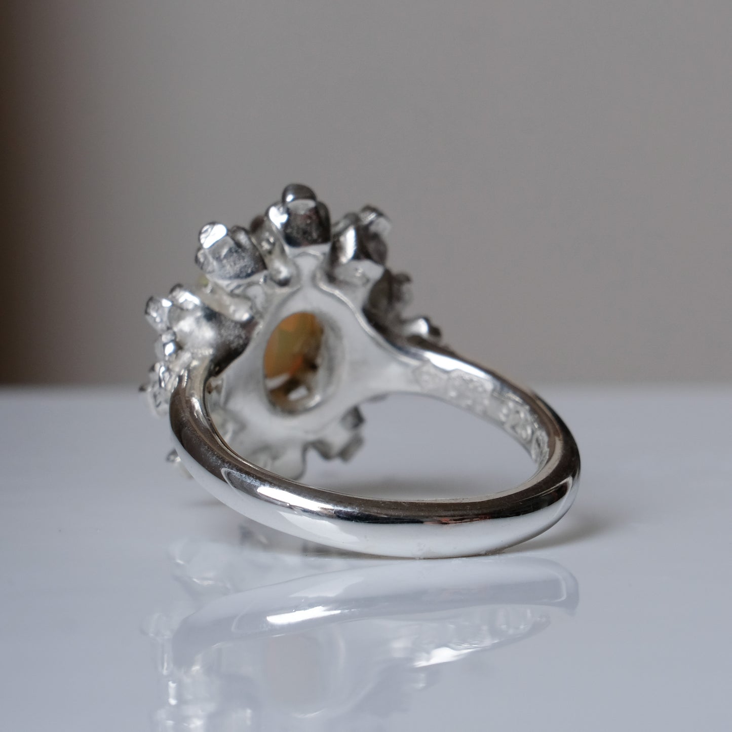 Silver ring with white opal gemstone in skull halo design on reflective background handmade in London, UK