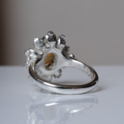 Silver ring with white opal gemstone in skull halo design on reflective background handmade in London, UK