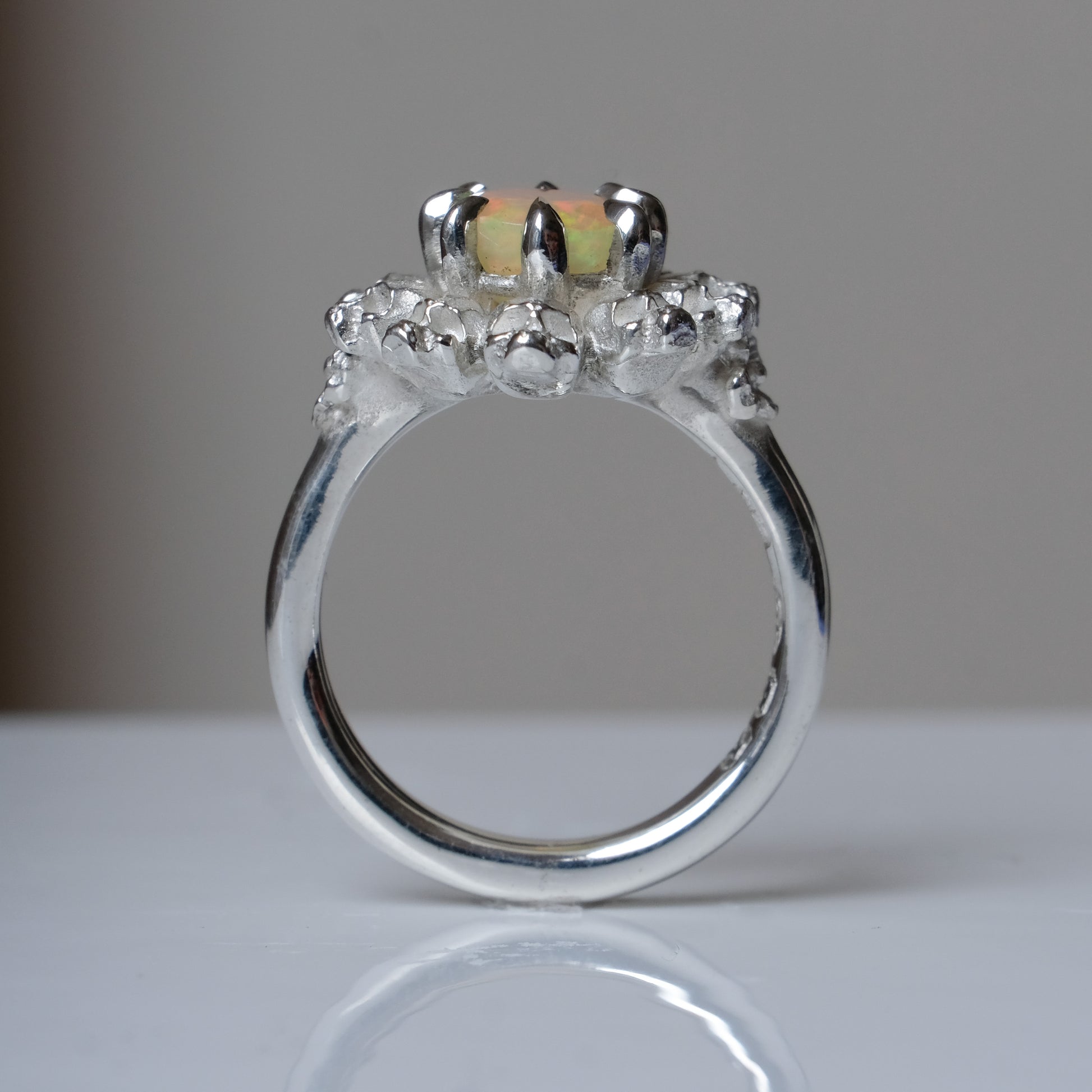 Silver ring with white opal gemstone in skull halo design on reflective background handmade in London, UK