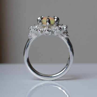 Silver ring with white opal gemstone in skull halo design on reflective background handmade in London, UK