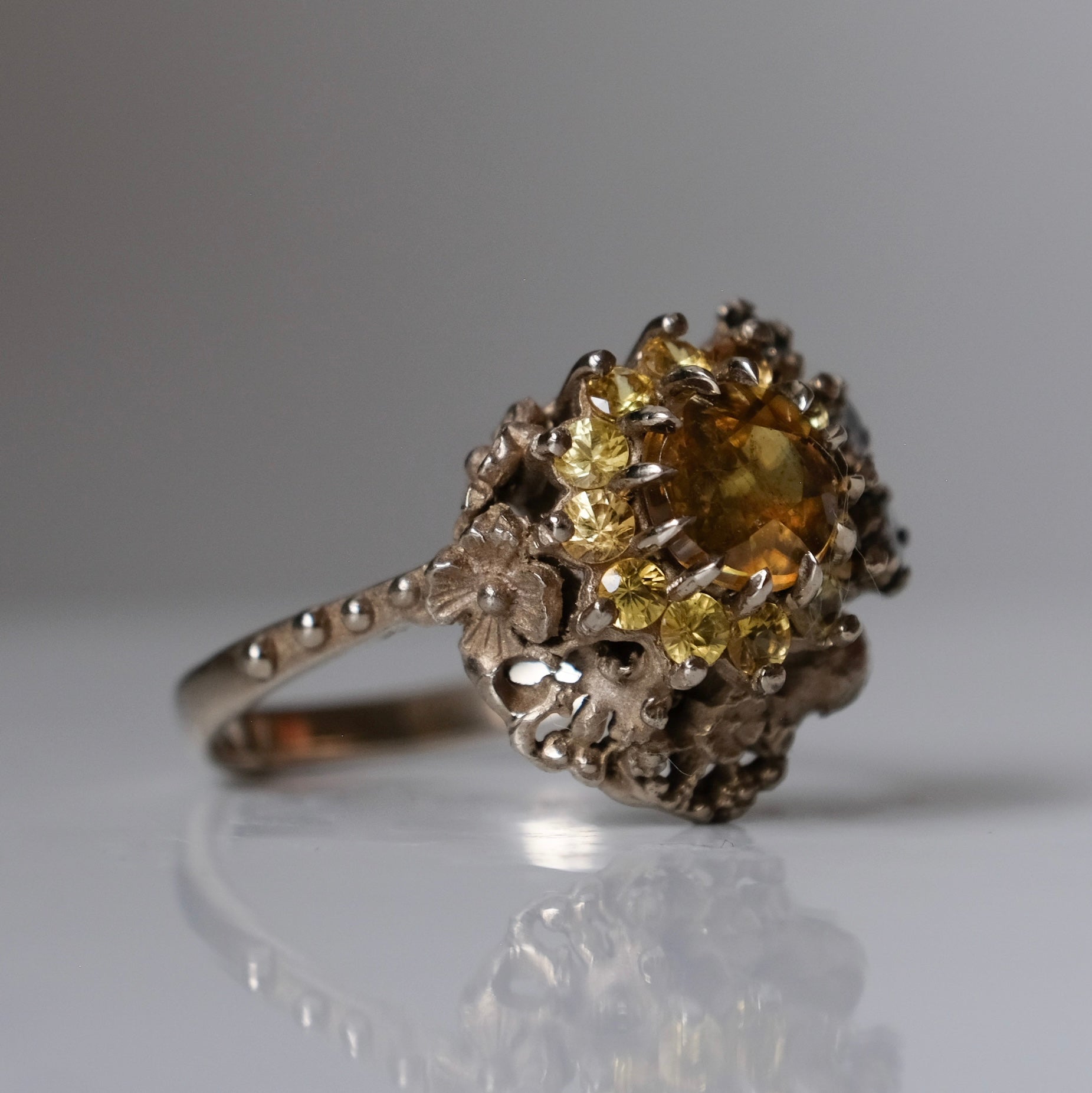 Salacia engagement ring with central Sphene and sapphire halo, salt and pepper diamonds, skulls and flowers. Made in 14ct white gold in London by Charlie Shires