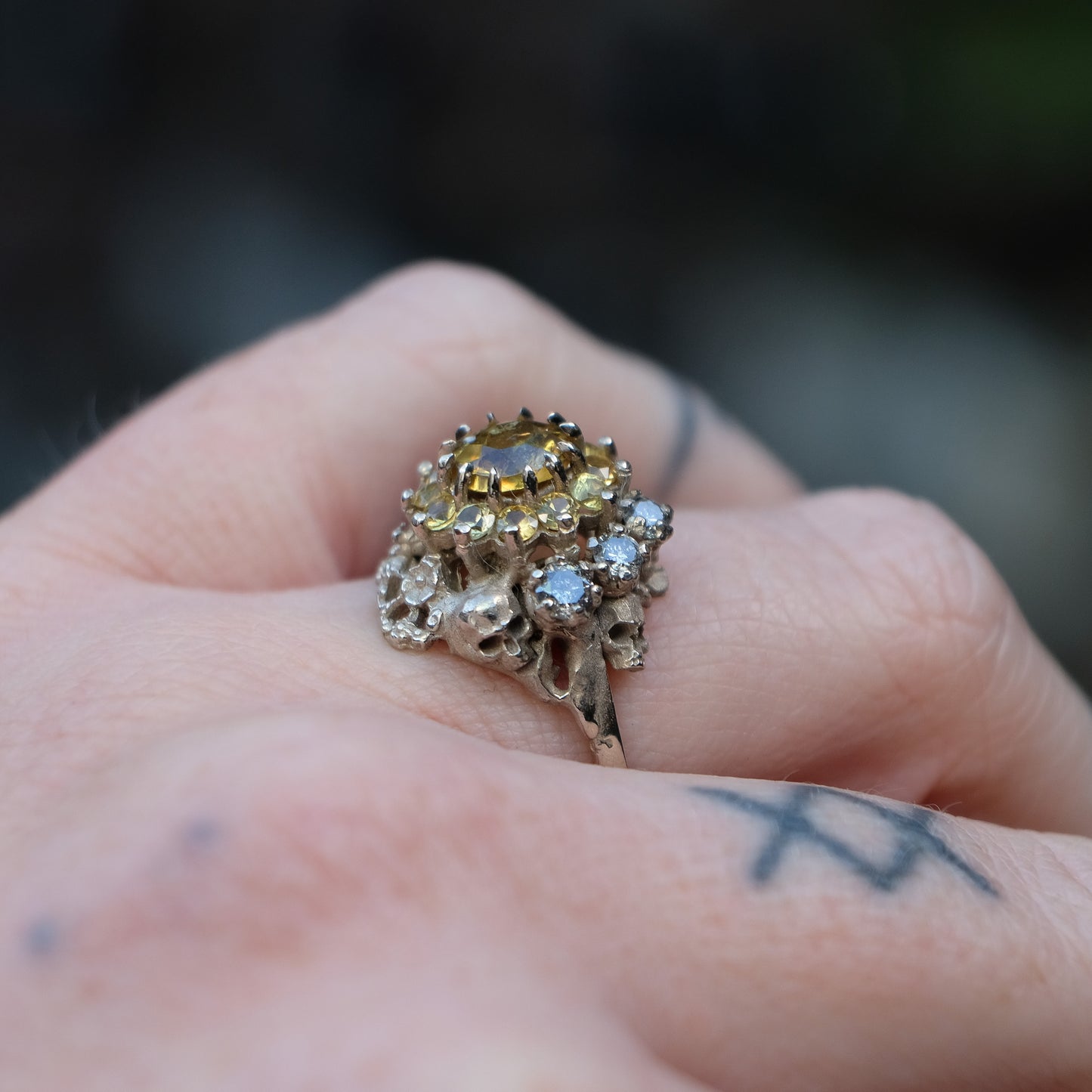 Salacia engagement ring with central Sphene and sapphire halo, salt and pepper diamonds, skulls and flowers. Made in 14ct white gold in London by Charlie Shires