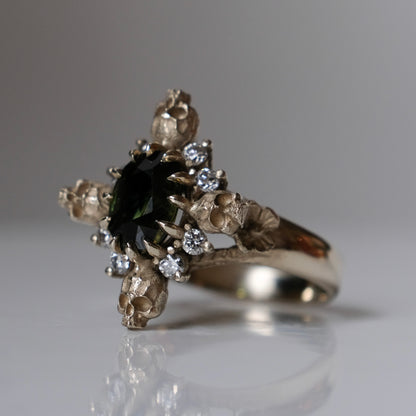 14ct white gold parti sapphire ring with halo of diamonds and skulls. Flowers flank the side of the band. Handmade in London by Charlie Shires