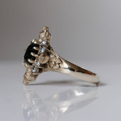 14ct white gold parti sapphire ring with halo of diamonds and skulls. Flowers flank the side of the band. Handmade in London by Charlie Shires