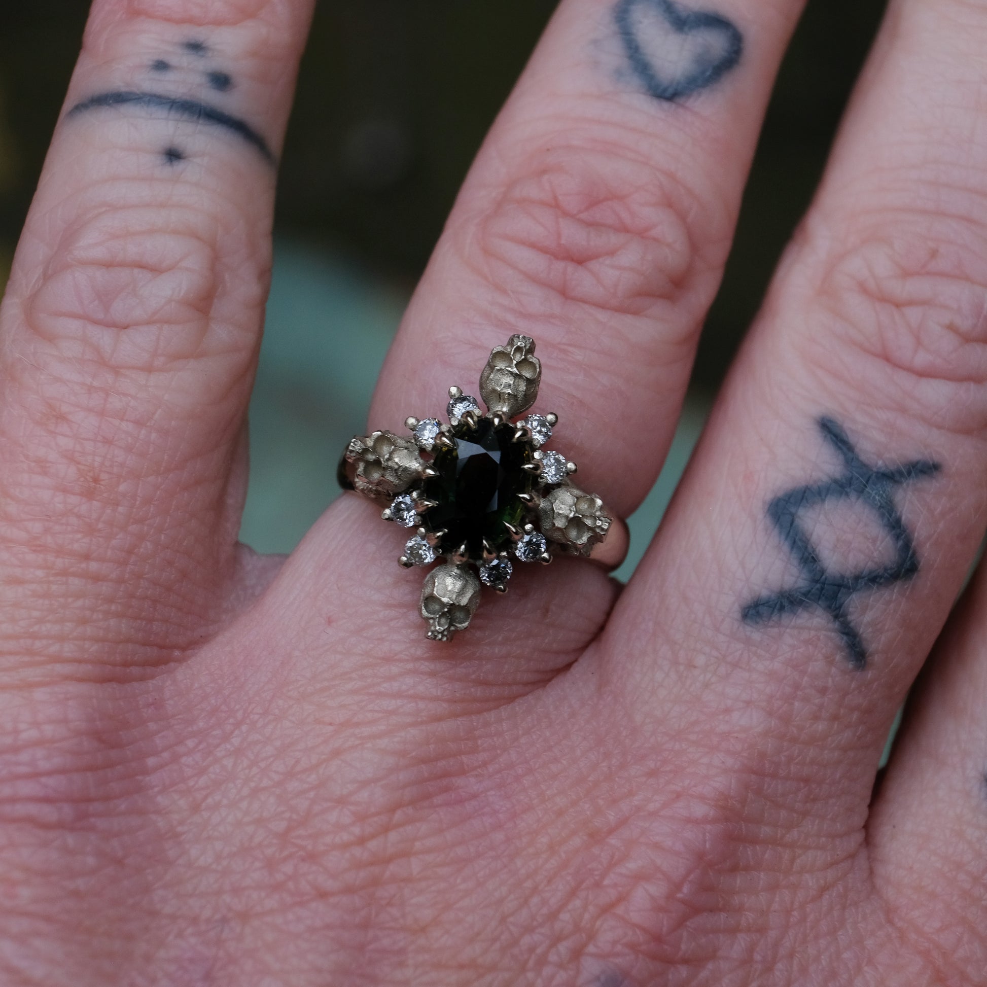 14ct white gold parti sapphire ring with halo of diamonds and skulls. Flowers flank the side of the band. Handmade in London by Charlie Shires