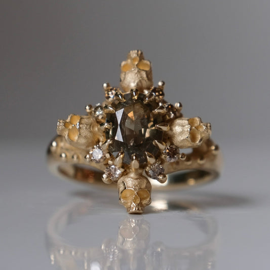9ct yellow gold engagement ring with unheated sapphire and champagne diamond halo decorated with 4 skulls. 
Handmade in London by Charlie Shires