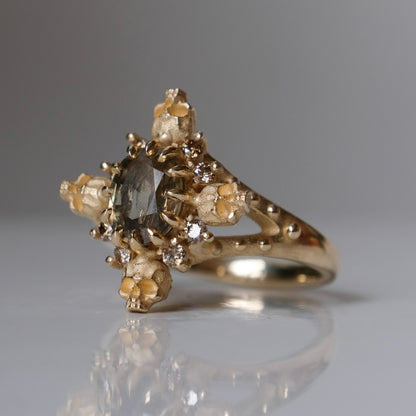 9ct yellow gold engagement ring with unheated sapphire and champagne diamond halo decorated with 4 skulls. 
Handmade in London by Charlie Shires