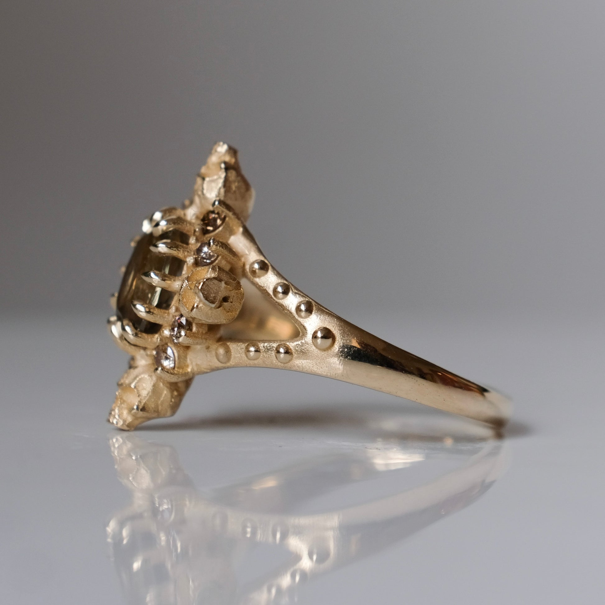 9ct yellow gold engagement ring with unheated sapphire and champagne diamond halo decorated with 4 skulls. 
Handmade in London by Charlie Shires