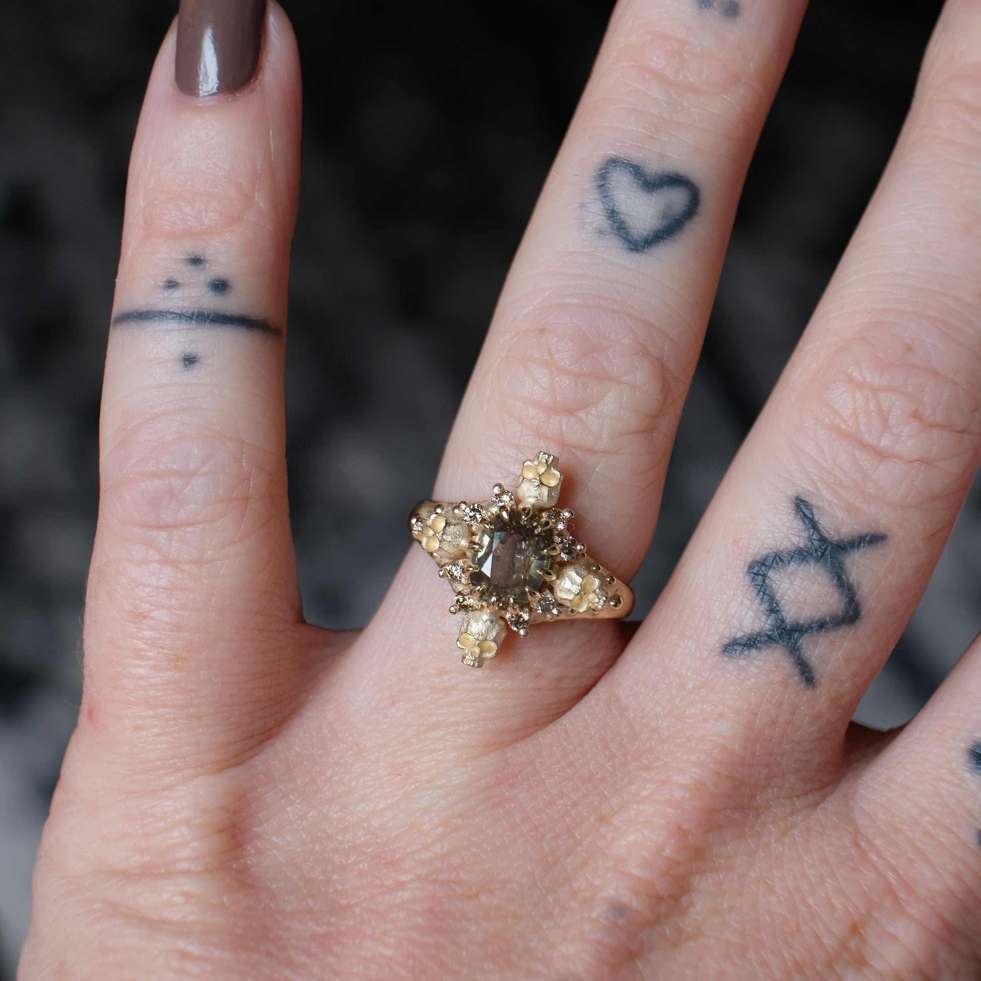 9ct yellow gold engagement ring with unheated sapphire and champagne diamond halo decorated with 4 skulls. 
Handmade in London by Charlie Shires