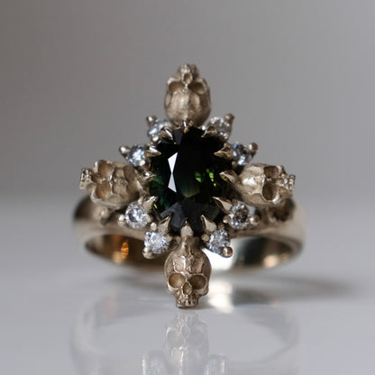 14ct white gold parti sapphire ring with halo of diamonds and skulls. Flowers flank the side of the band. Handmade in London by Charlie Shires