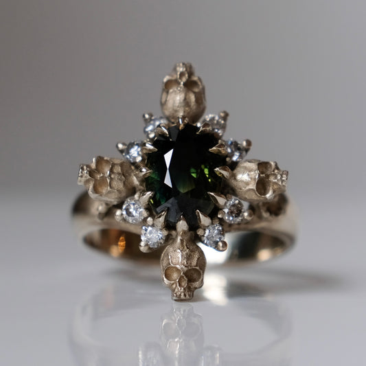 14ct white gold parti sapphire ring with halo of diamonds and skulls. Flowers flank the side of the band. Handmade in London by Charlie Shires