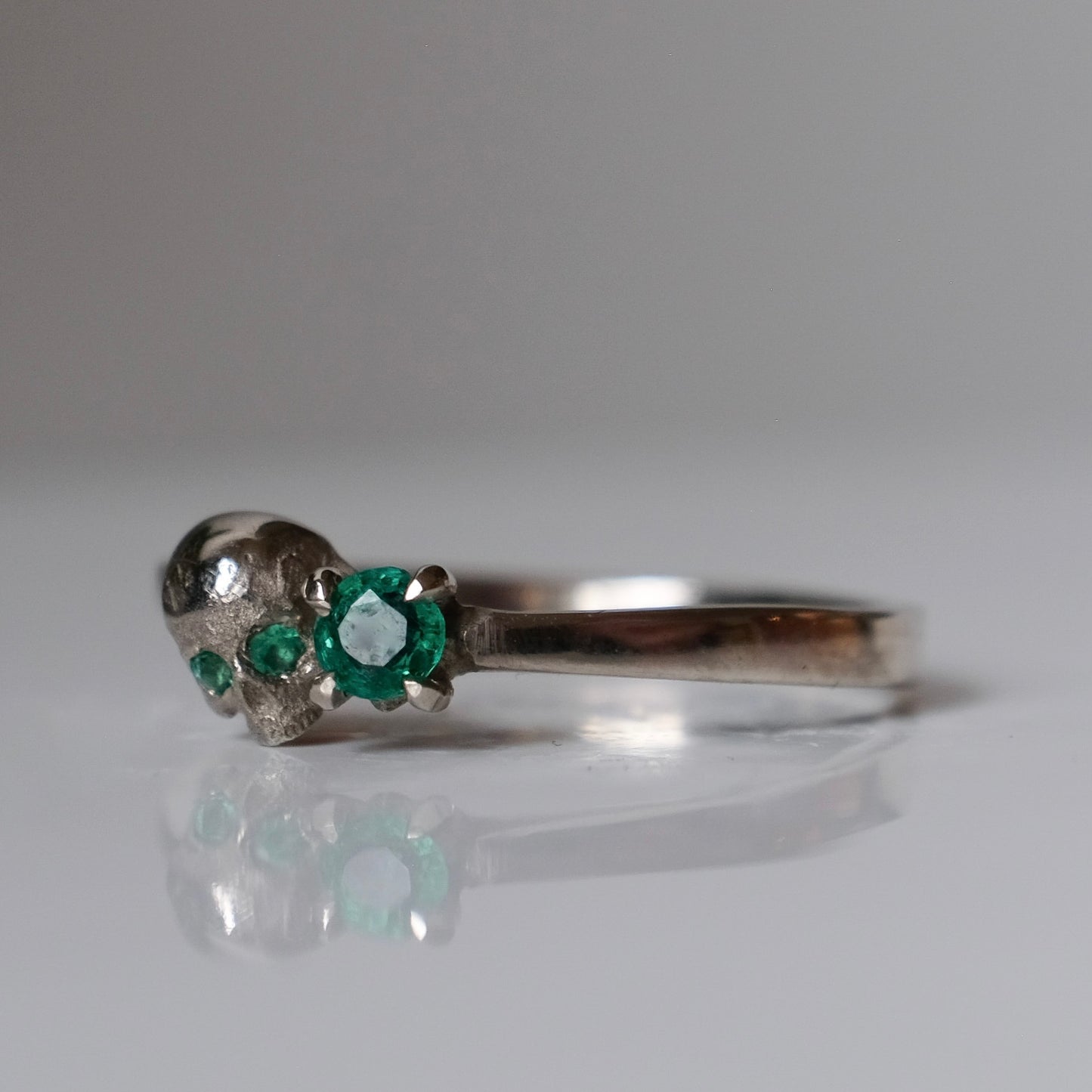 14ct white gold engagement ring with skull and emerald claw set stone. Handmade in London by Charlie Shires