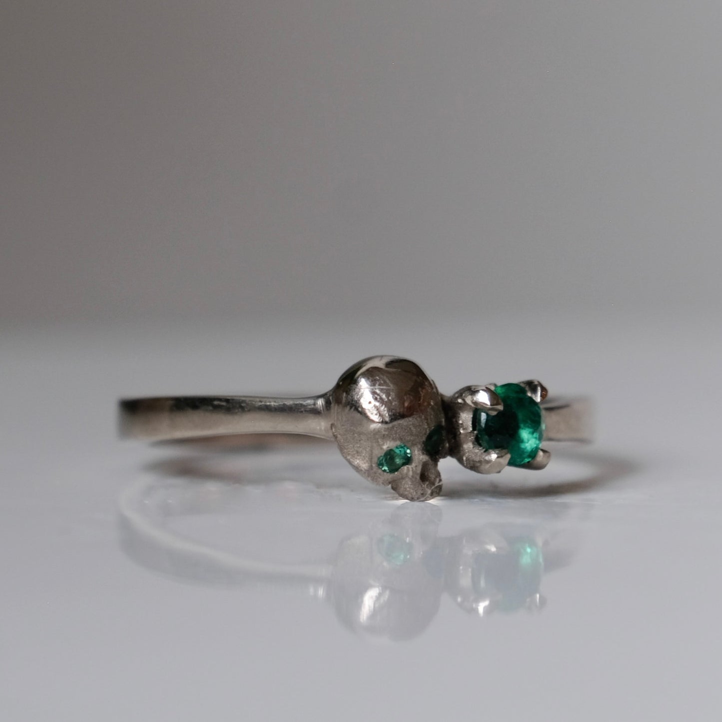 14ct white gold engagement ring with skull and emerald claw set stone. Handmade in London by Charlie Shires