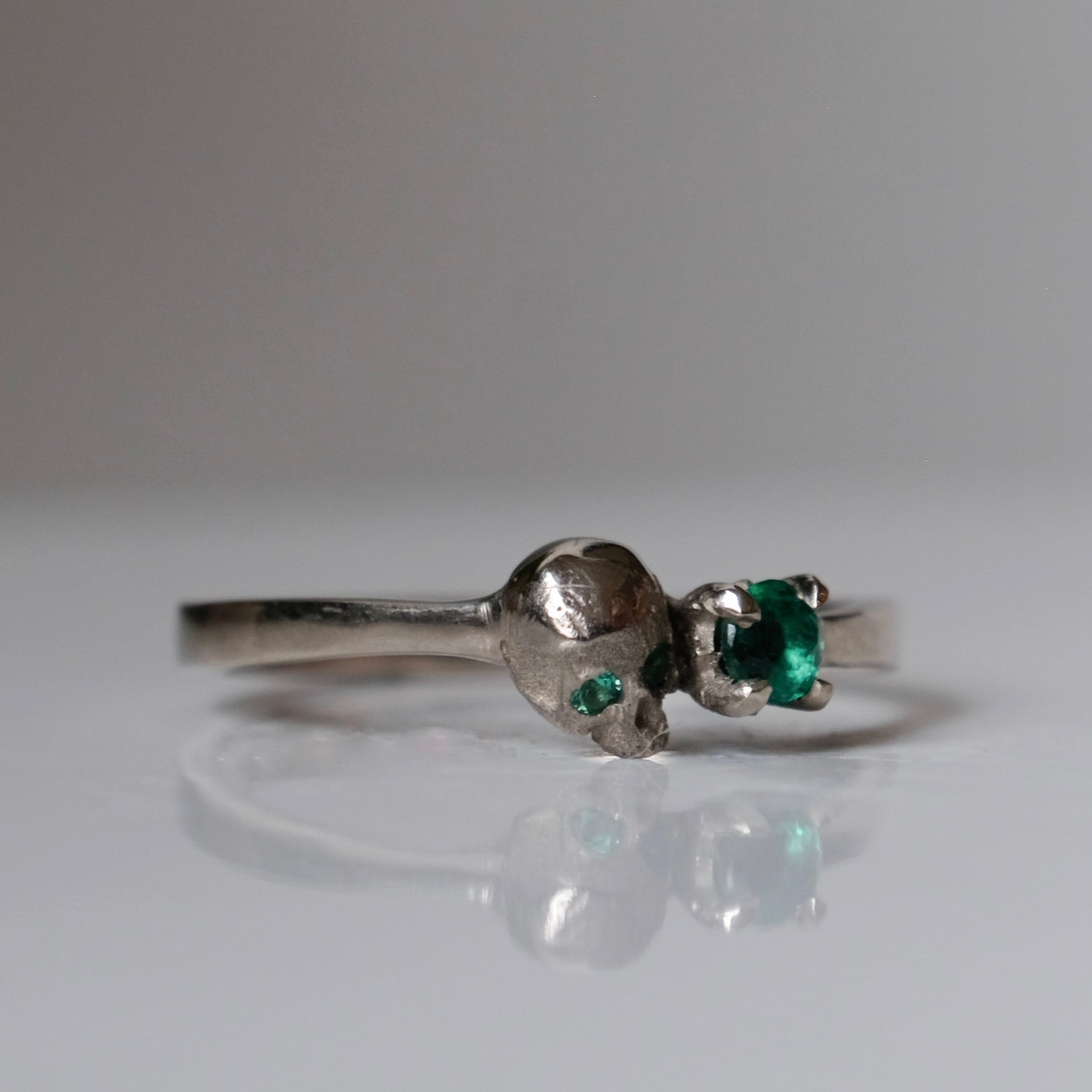 14ct white gold engagement ring with skull and emerald claw set stone. Handmade in London by Charlie Shires