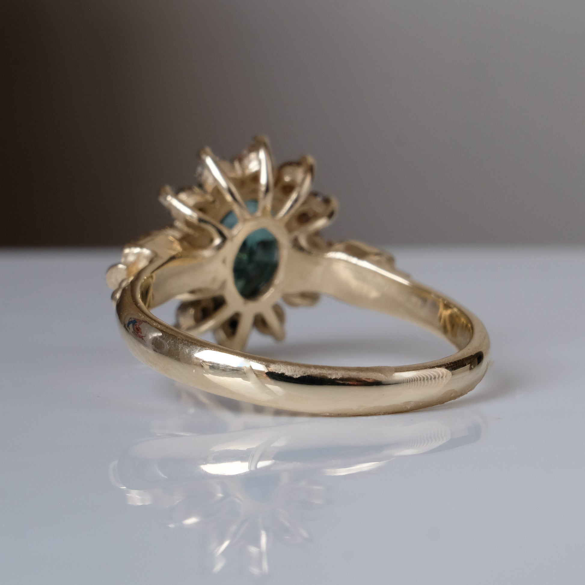 Montana sapphire ring with champagne diamonds in a halo/cluster setting, flanked by two skulls. Handmade in 9ct yellow gold on a white background. Handmade in London by Charlie Shires from recycled metals.