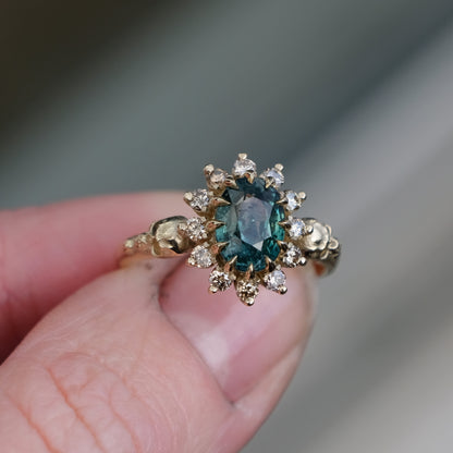 Montana sapphire ring with champagne diamonds in a halo/cluster setting, flanked by two skulls. Handmade in 9ct yellow gold on a white background. Handmade in London by Charlie Shires from recycled metals.