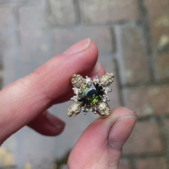 14ct white gold parti sapphire ring with halo of diamonds and skulls. Flowers flank the side of the band. Handmade in London by Charlie Shires