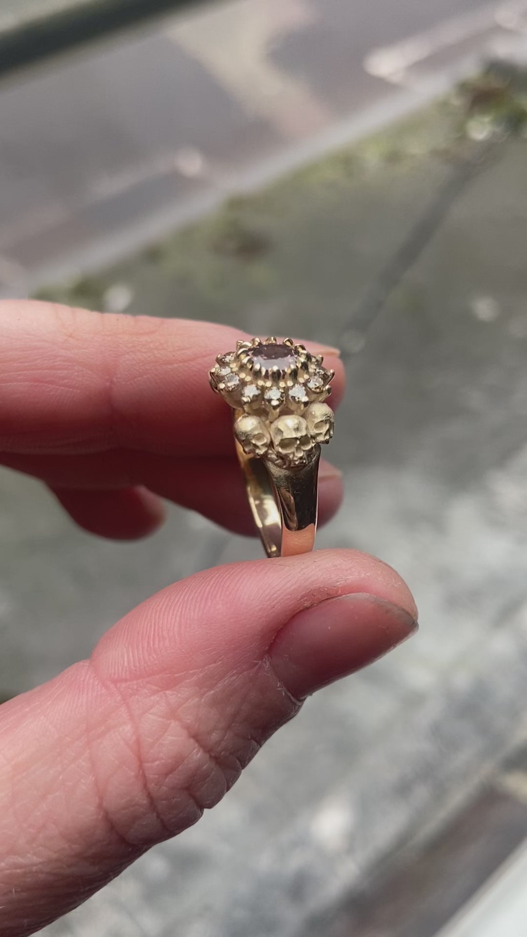 9ct yellow gold engagement ring with central colour change garnet and a champagne diamond halo. 6 skulls flank the side of the setting. 
Handmade in London by Charlie Shires